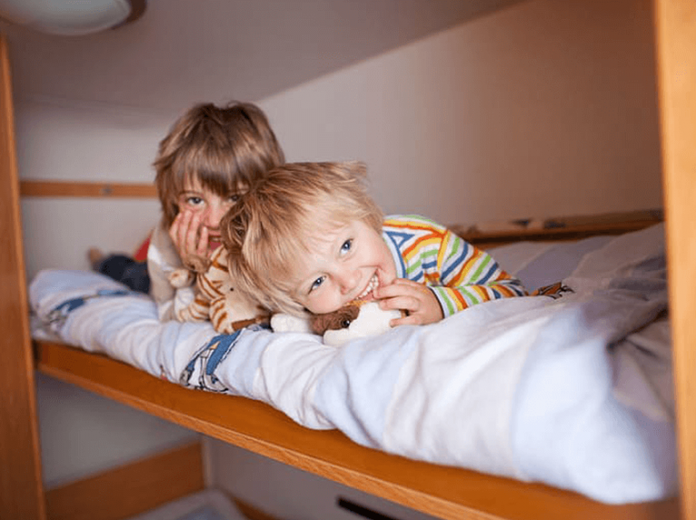 באנר של שני ילדים הנמצאים על מיטת קומותיים מחייכים